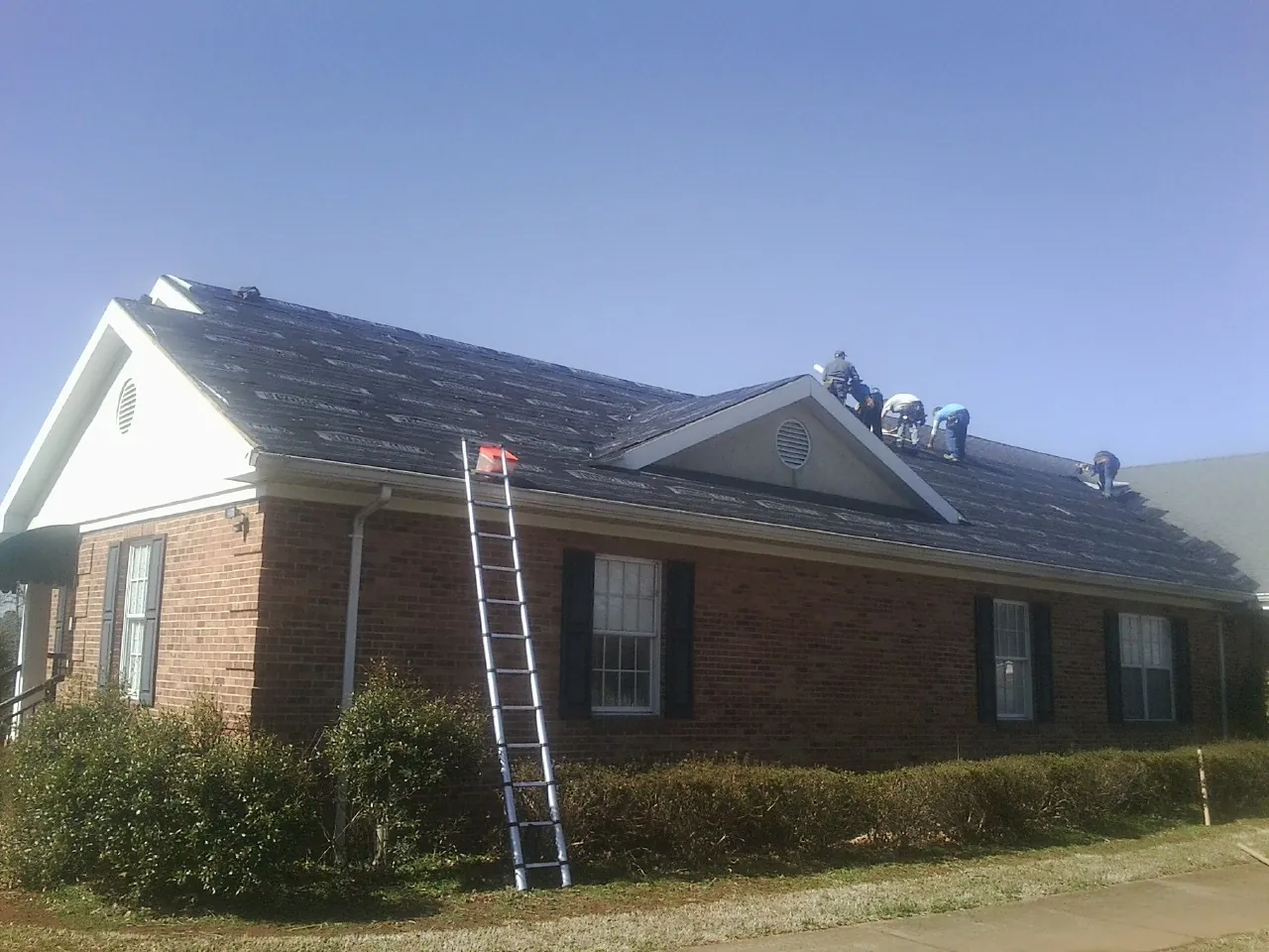 Crew tearing shingles off a brick ranch roof with a ladder set — Metal Roof Repair work by our crew in Eastport
