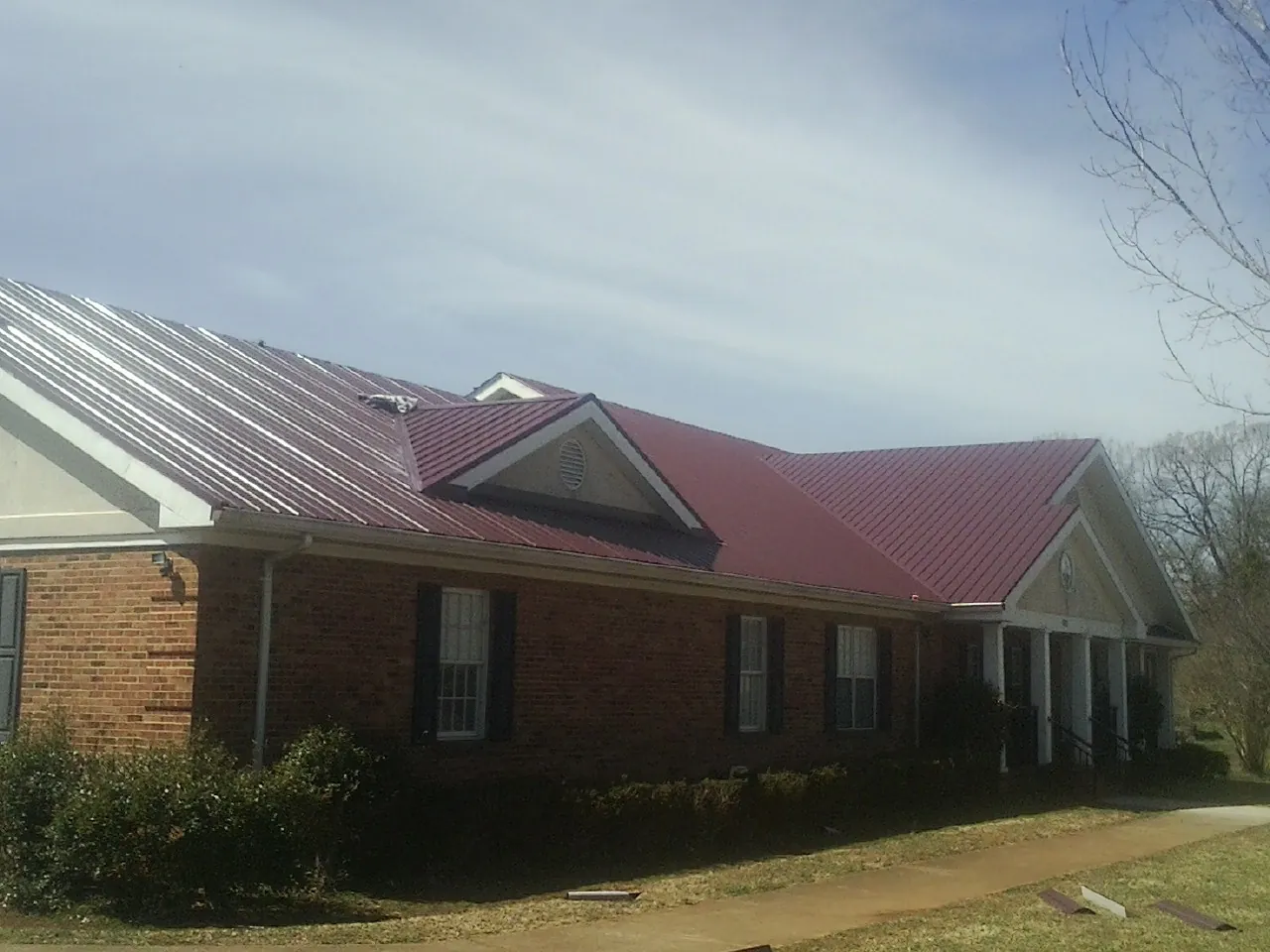Red metal roof with gabled entries on a long brick building, from a Hail Damage Roof Repair job in Eastport