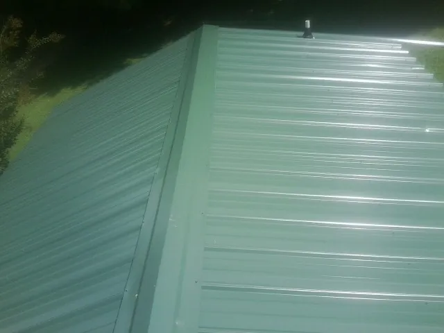 New green metal panels meeting at the ridge of a roof — Flat Roof Repair work by our crew in Eastport